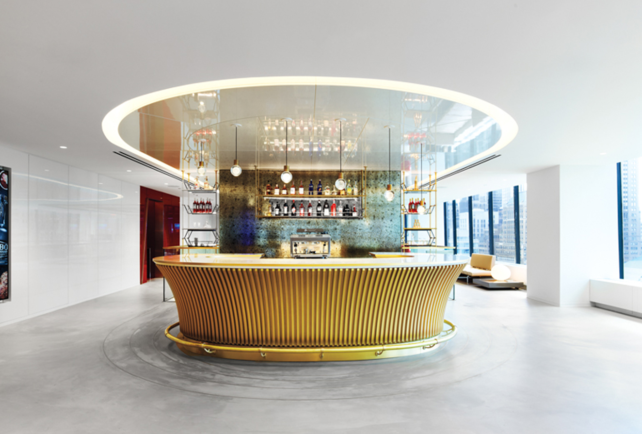 ELAI Circular gold bar centerpiece at Campari New York HQ, designed by Gensler, with glass shelves, metallic backsplash, white surroundings, and city views